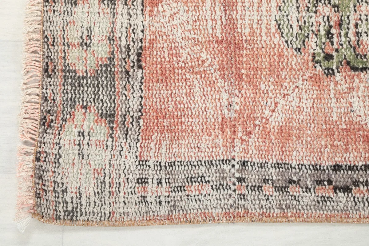 Close-up of the rug's border and fringe, showing the charcoal and gray patterns and the faded rose field.