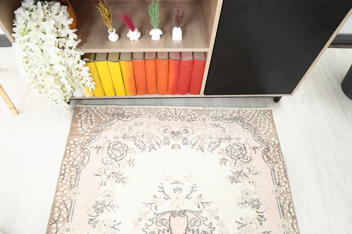 Detailed angle view of the rug's top portion, revealing the beige border and pink field with motifs.