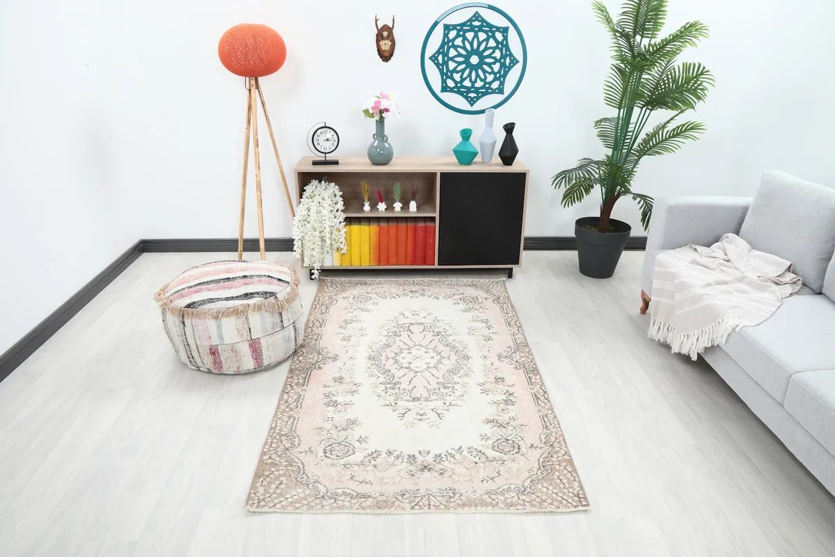 Vintage pink and cream area rug styled in a modern living room setting with a light gray sofa and wooden cabinet.