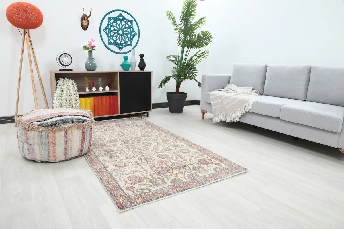 Angle view of the ivory and rose floral rug in a modern living space with a decorative pouf and plant