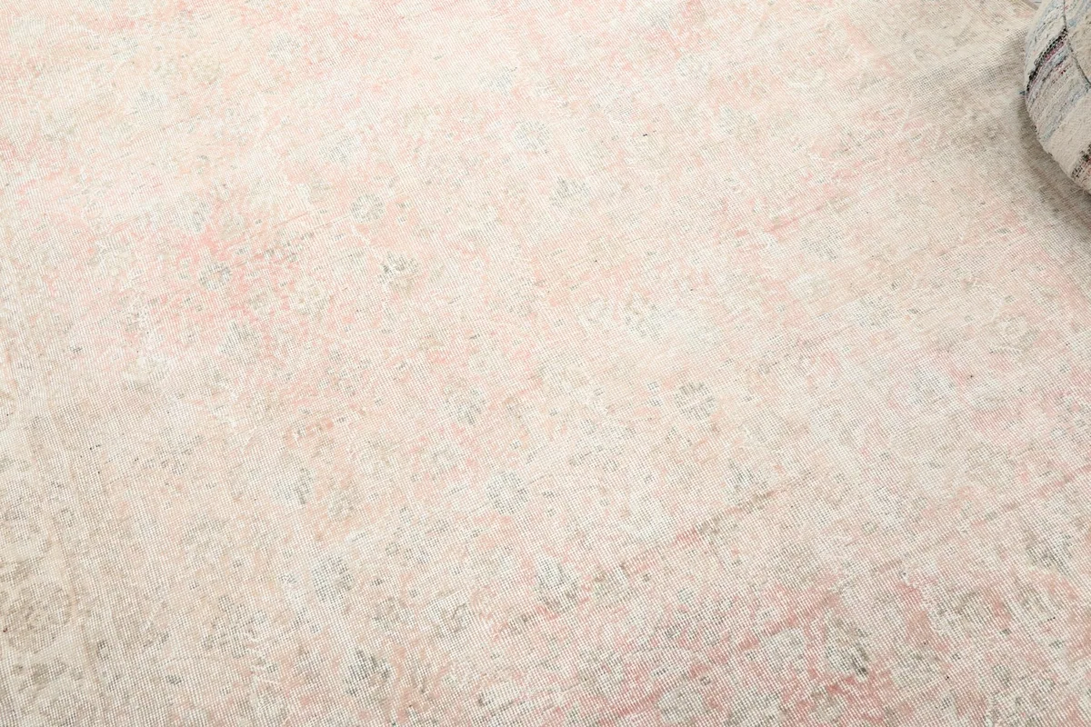 Detailed view of the rose and ivory rug's faded floral and geometric pattern with visible wool texture.