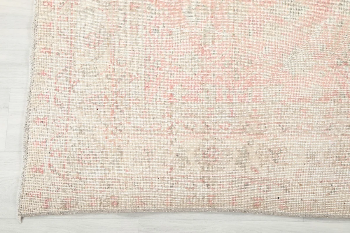 Detail of the rug's border, showcasing the faded rose and ivory geometric and floral motifs.