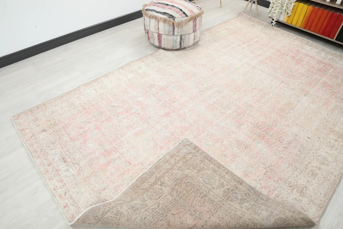Corner of the rose and ivory rug folded back, revealing the reverse side and its hand-knotted structure.