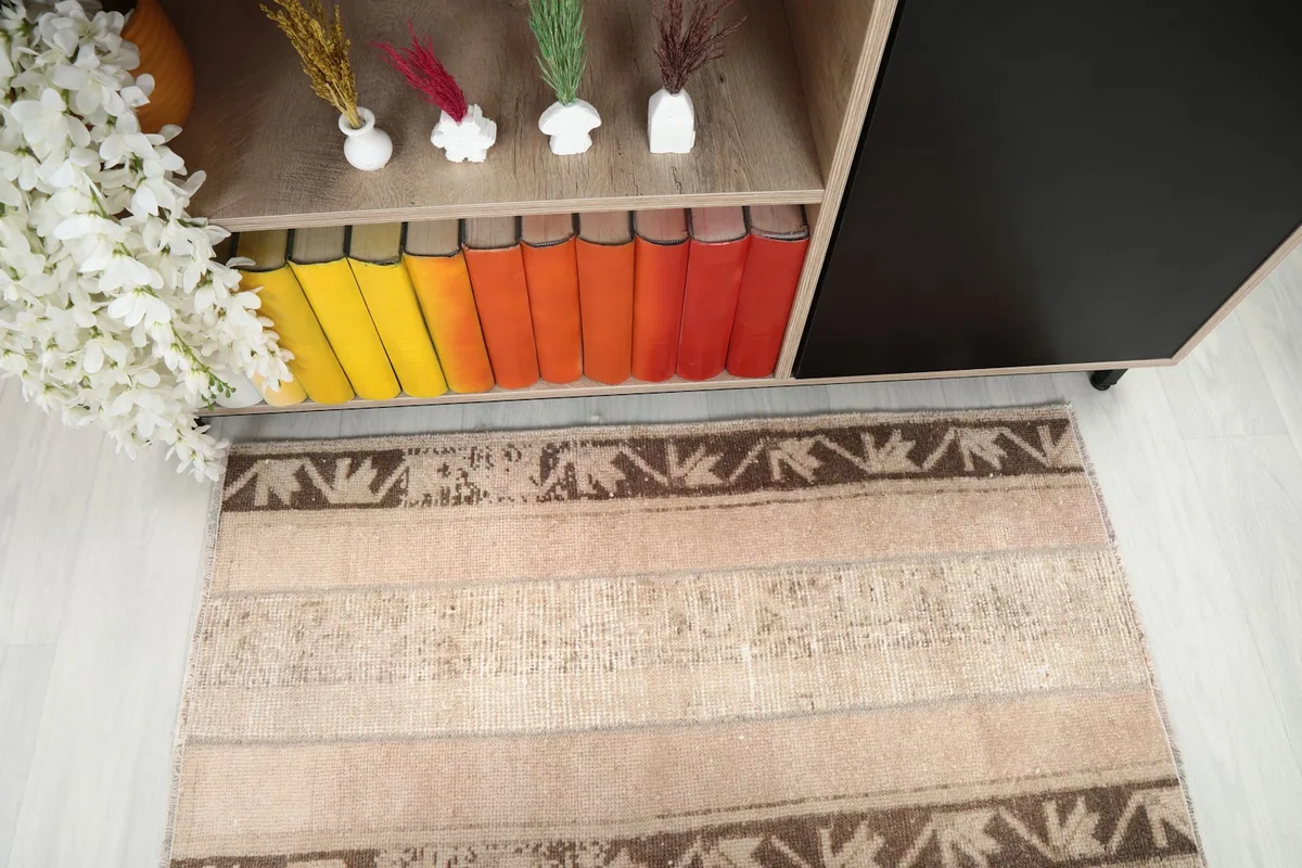 Angled view of the rug's surface, highlighting the tan field and brown tribal patterns.