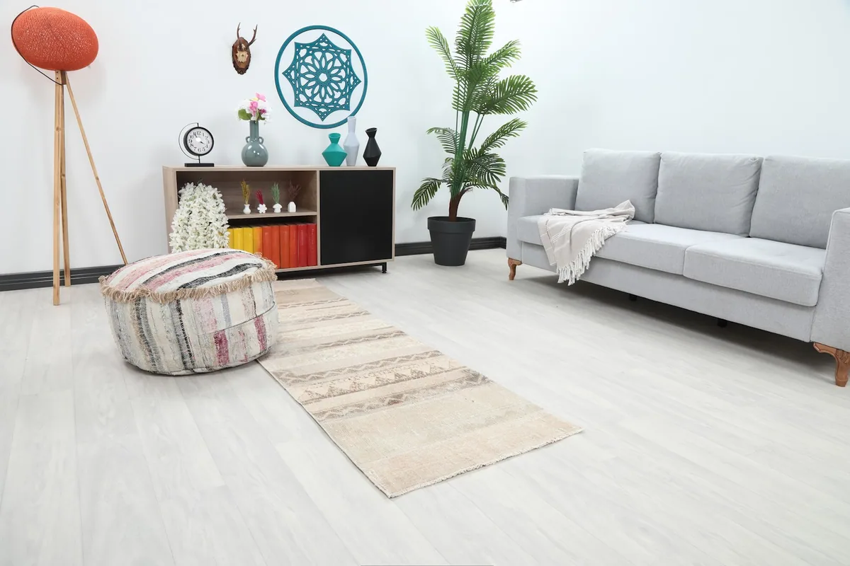 Tan and beige runner rug extending from a colorful pouf towards a gray sofa in a contemporary living space