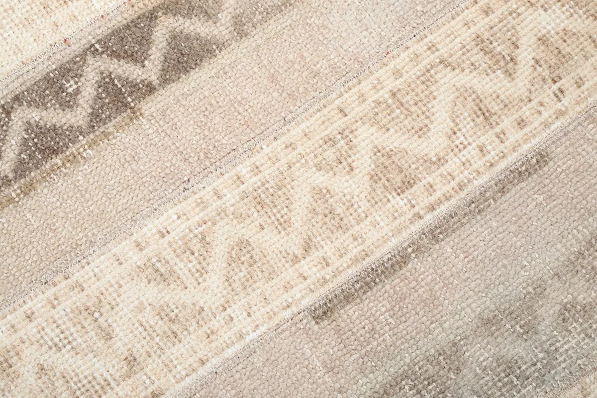 Close-up detail of the hand-knotted wool pile and faded geometric designs in beige and tan tones