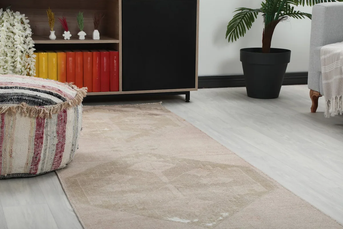 Close-up of the runner rug's rose and beige patterns beside a striped ottoman and wooden cabinet