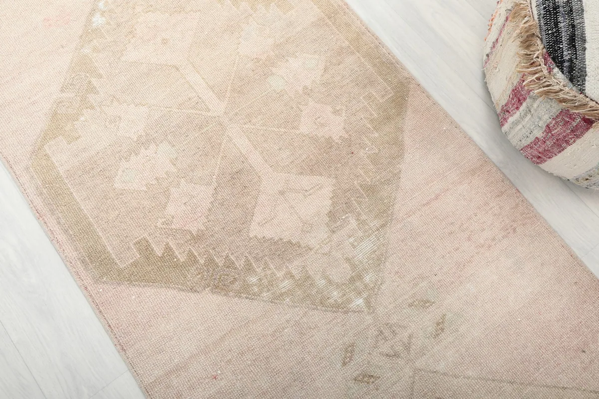 Detailed view of the rose and beige geometric motifs and natural patina on the vintage runner rug