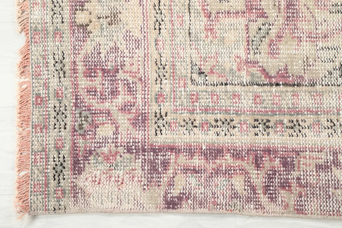 Corner detail of the rug, showcasing the intricate purple and ivory border patterns and short fringes