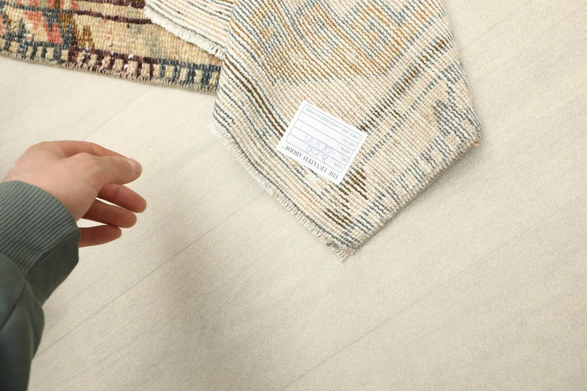 A hand holding a label near the back of the rug, showing the quality and origin tag.