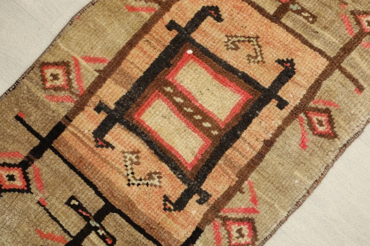 Close-up view of the central geometric motif in rose and black against the tan background.