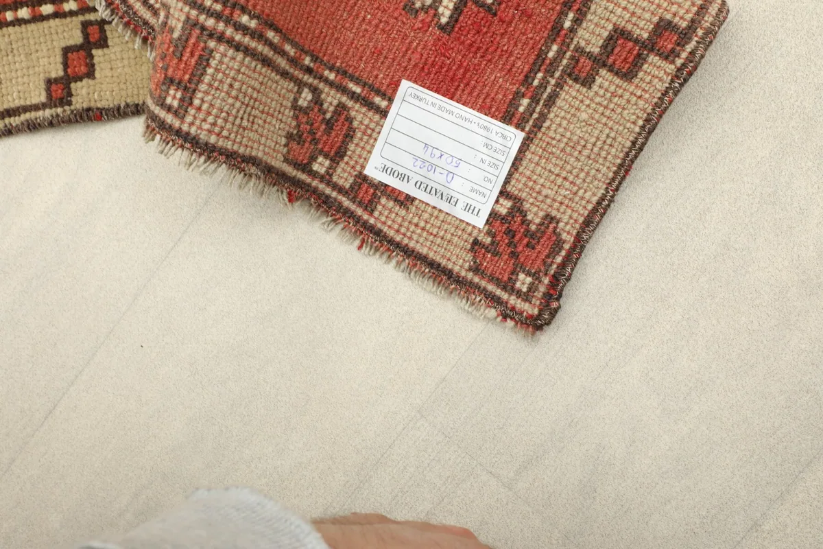 View of the rug with a label, demonstrating its small size next to a foot