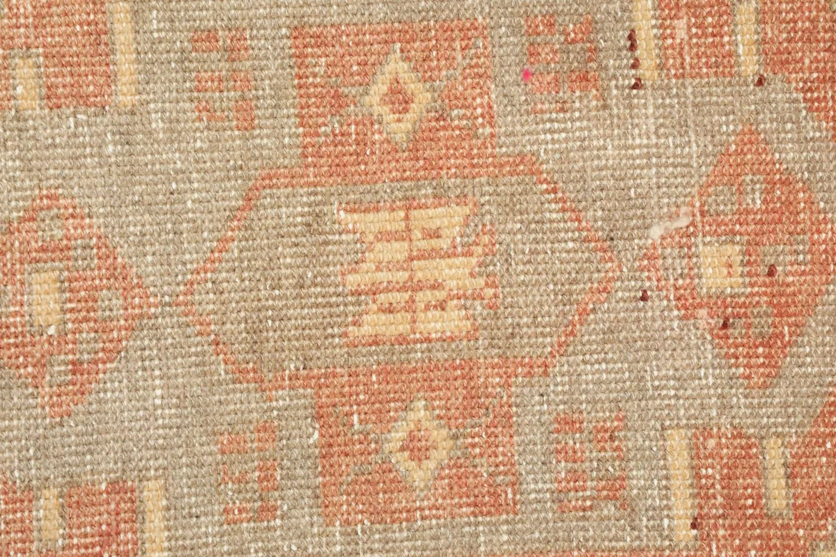 Close-up detail of the central tribal motif in rust and ivory on a beige field.
