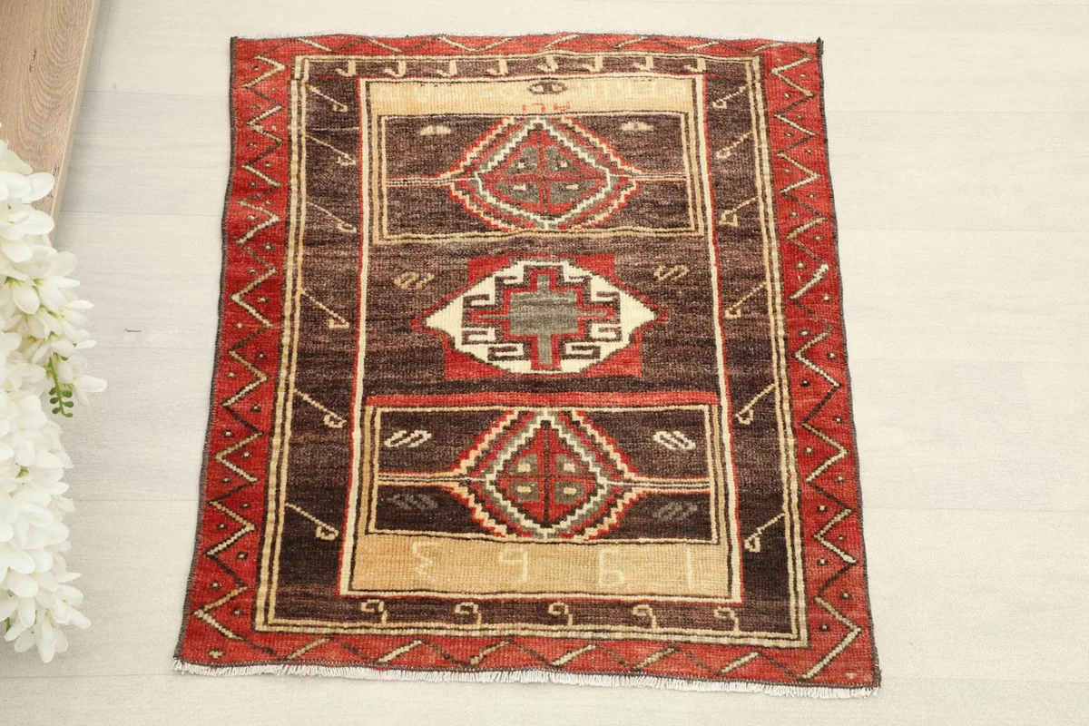 Overhead view of the vintage doormat, showcasing its central brown and beige field with red tribal motifs.