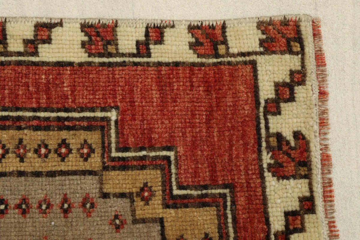 Detail view of the rug's edge, showing the red field meeting the beige border and inner patterns.