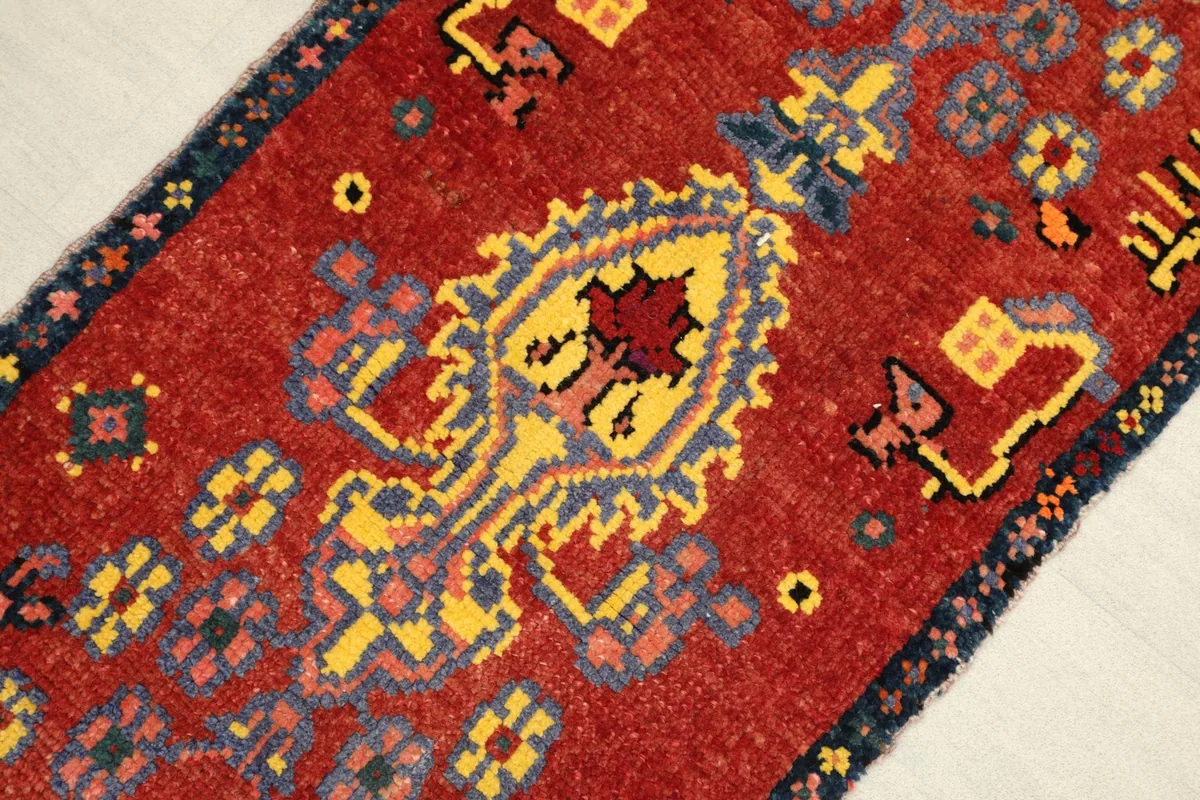 Angled view highlighting the red field, yellow and navy patterns, and the texture of the low pile.