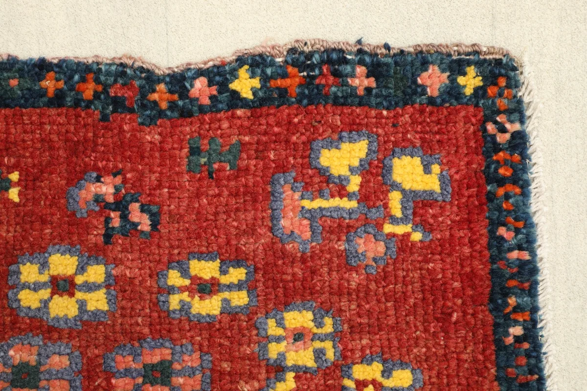 Detailed view of the rug's border and a section of the red field with small tribal motifs.