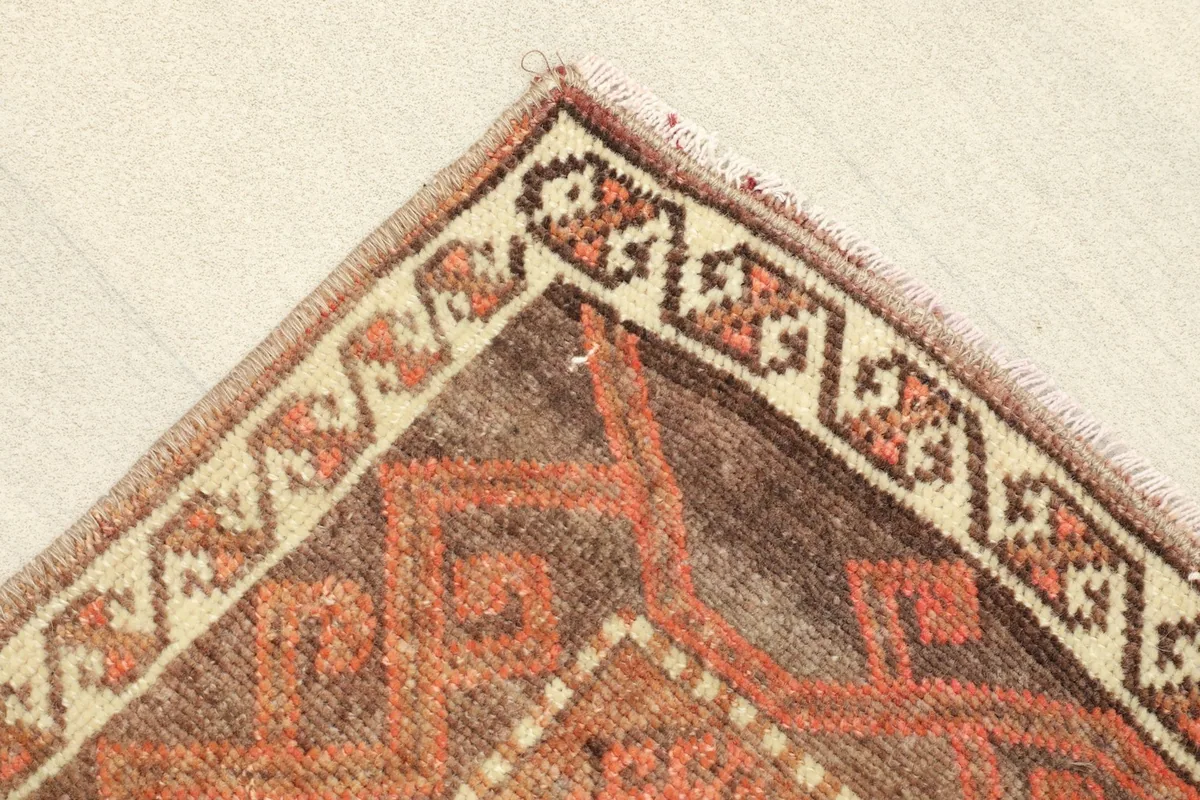 Corner view showing the beige border with small geometric motifs and the primary rust and brown field
