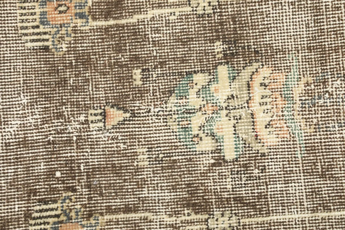 Close-up detail of the hand-knotted wool pile and beige, blue, and pink motifs on the brown field.