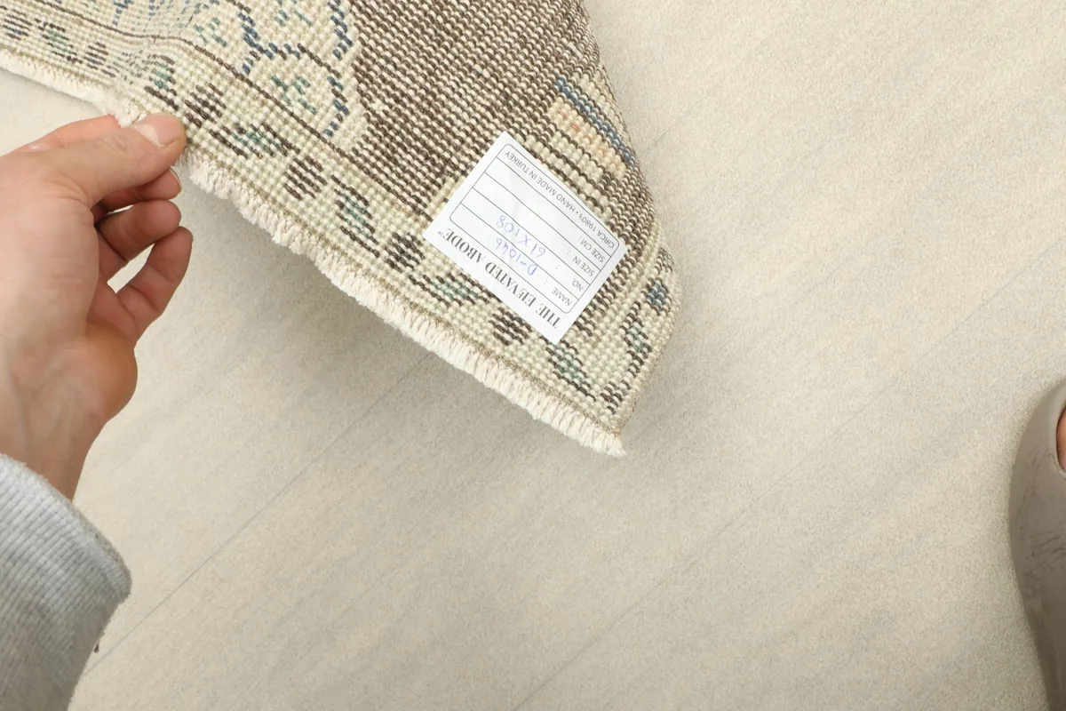 Hand holding a corner of the rug, showing the short fringe and the professionally cleaned label.