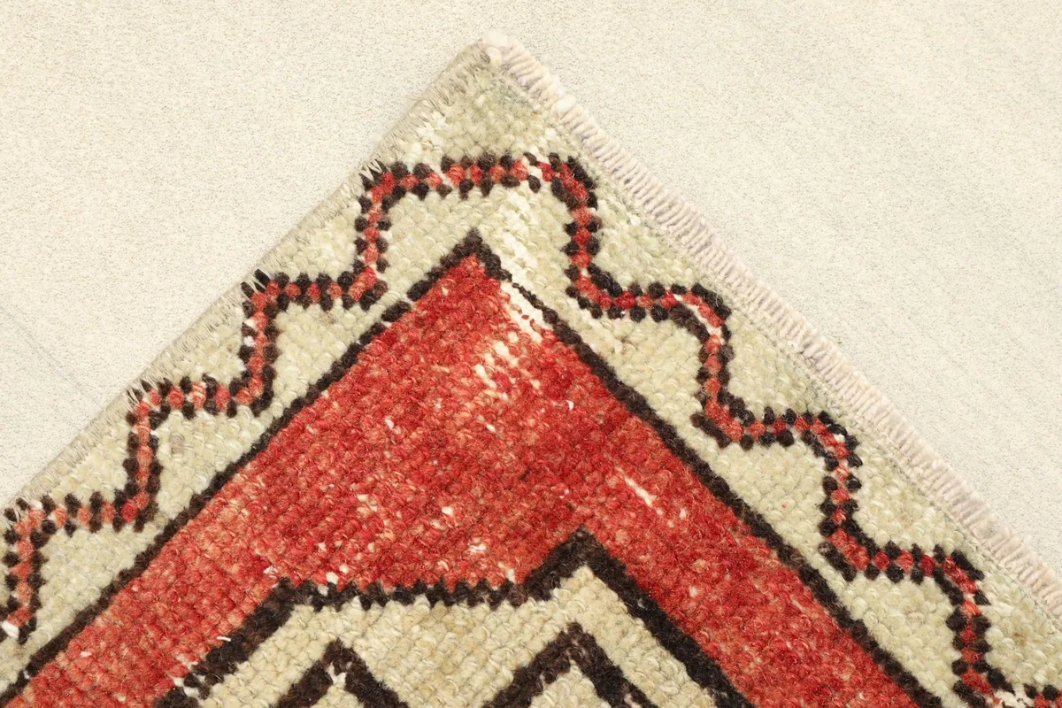 Corner detail of the rug showing the ivory border with a rust and black zigzag pattern.