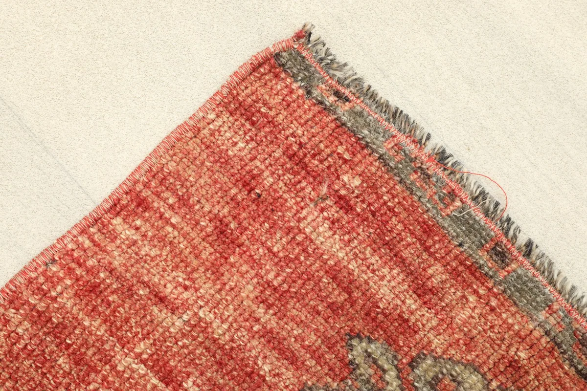 Corner detail showing the edge finishing and the textured rust colored field of the rug.