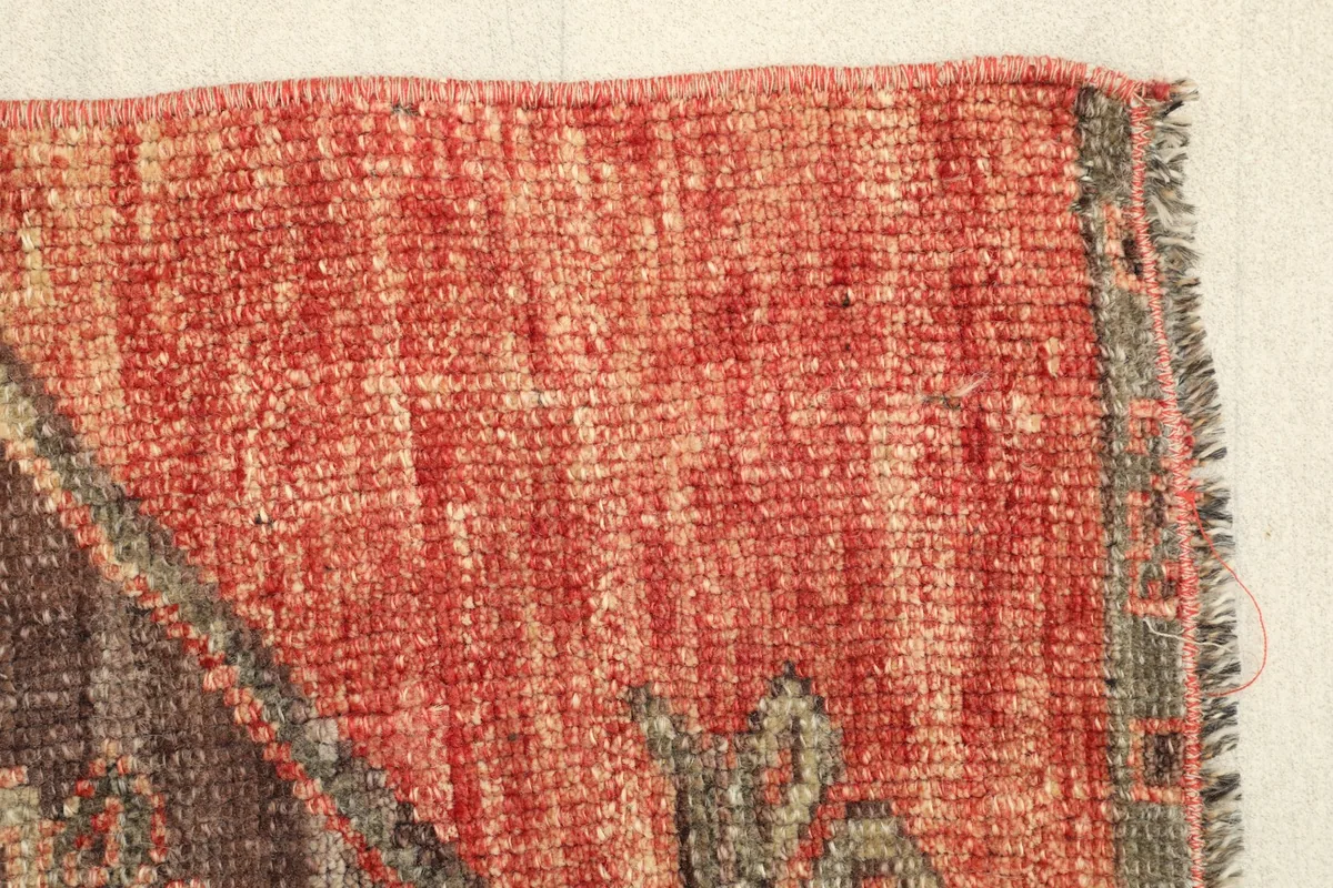 Edge of the rug displaying the subtle border design and the varying shades within the rust field.