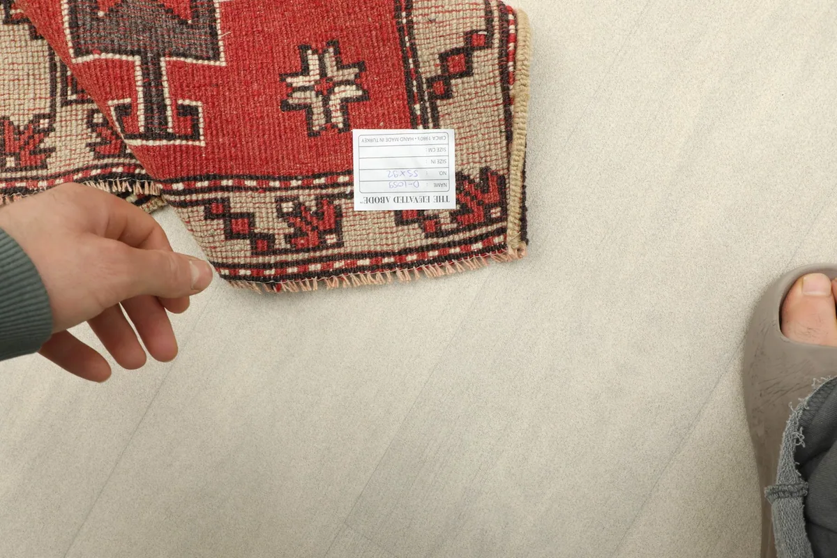 Underside of the rug with a hand visible, showing the woven cotton foundation and short fringes.