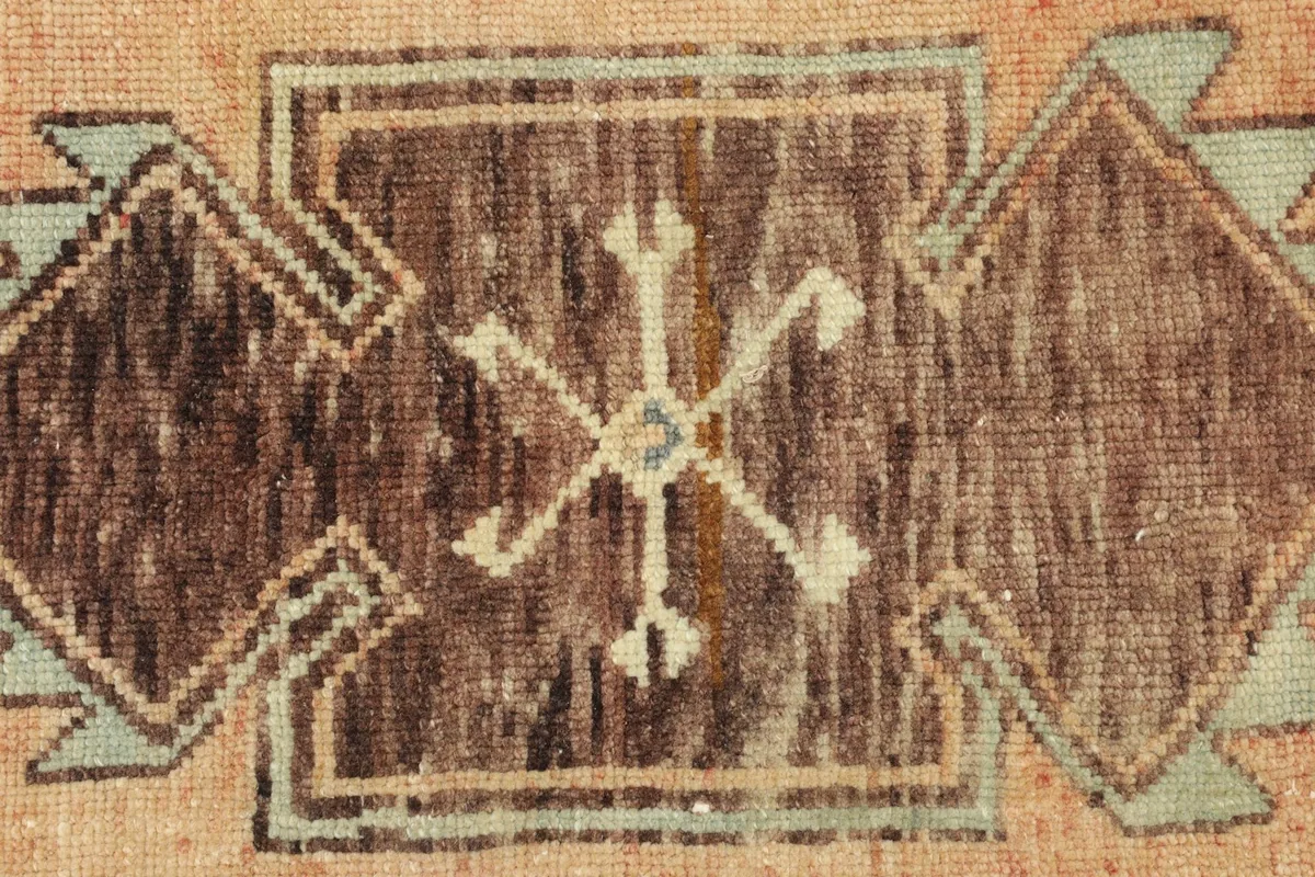 Macro detail of the hand-knotted wool pile and tribal symbols in brown, beige, and olive.
