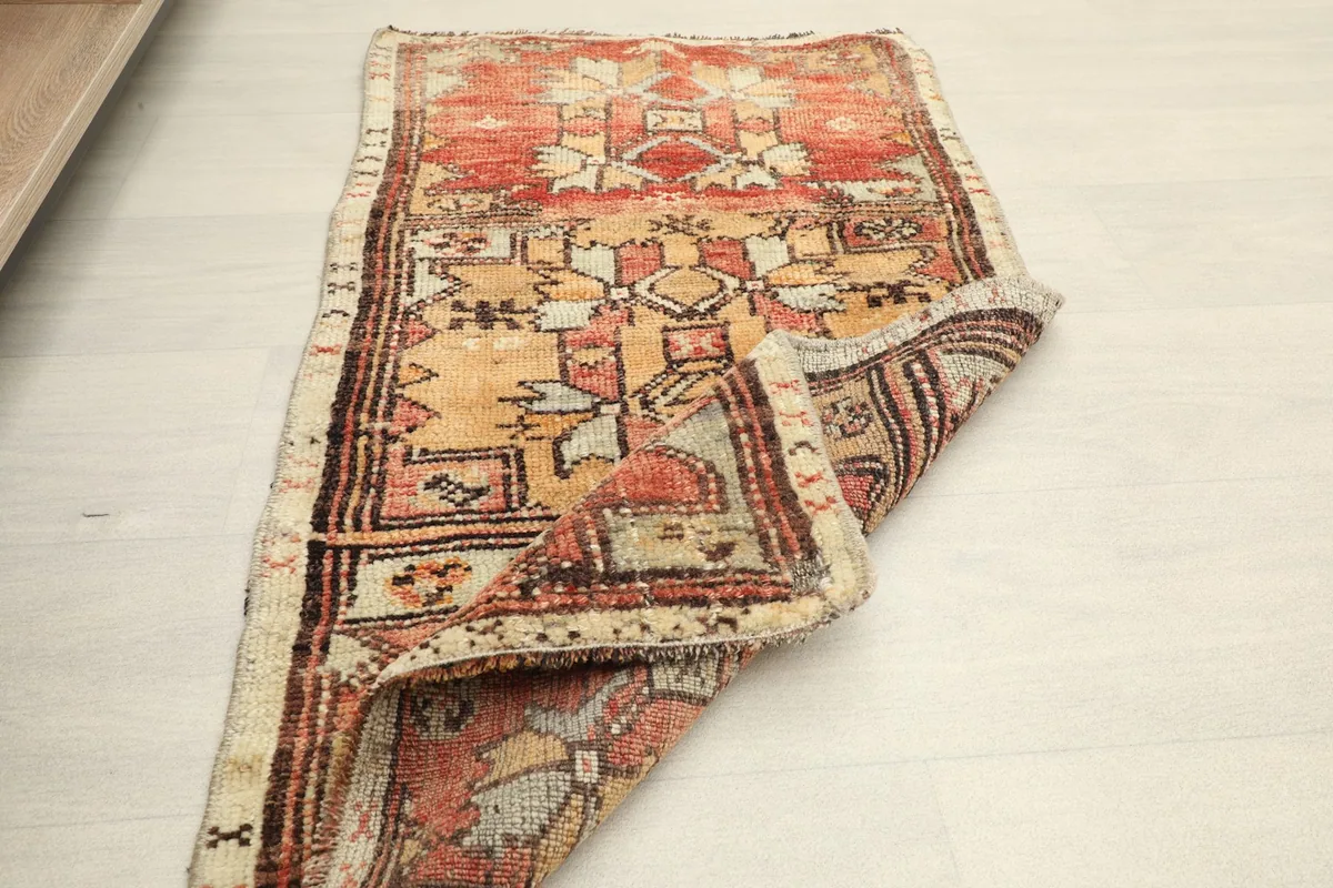 The small vintage rug partially folded on a light floor, suggesting its use in a home setting