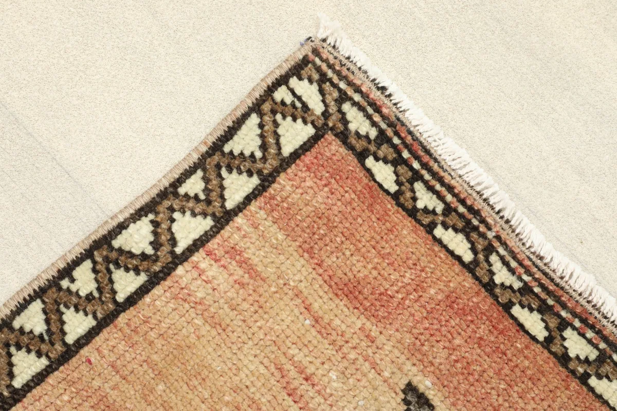 Corner view showing the patterned border in beige and brown, and the subtle fringe of the rug.