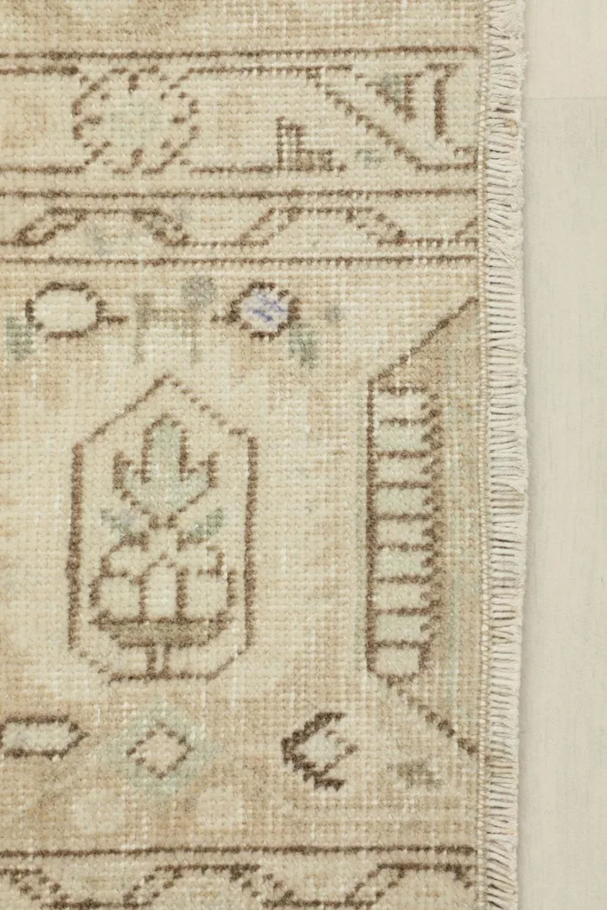 Close-up detail of the rug's beige field, brown motifs, and subtle green and purple accents near the fringe.