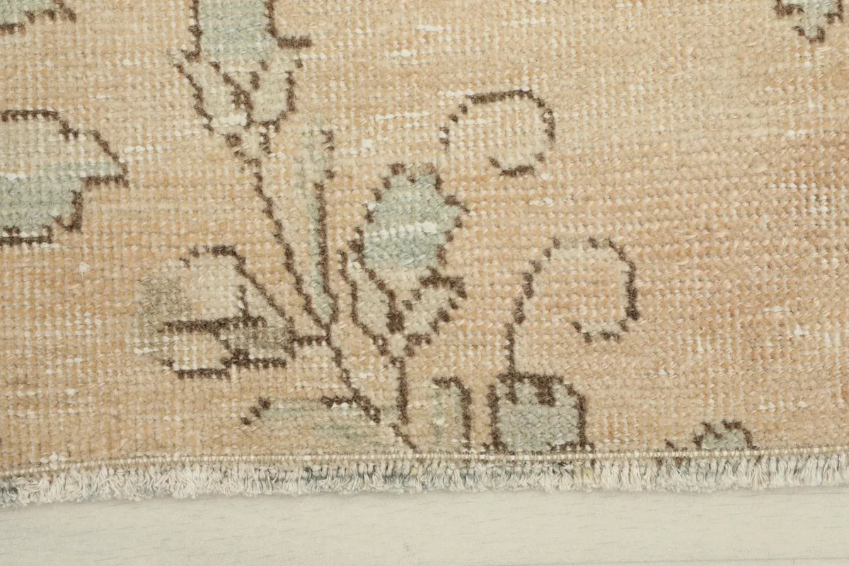 Close-up detail of the rug's floral motifs in olive and brown on the tan field