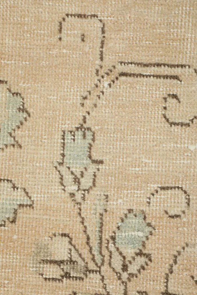 Macro shot highlighting the hand-knotted texture and muted olive floral elements