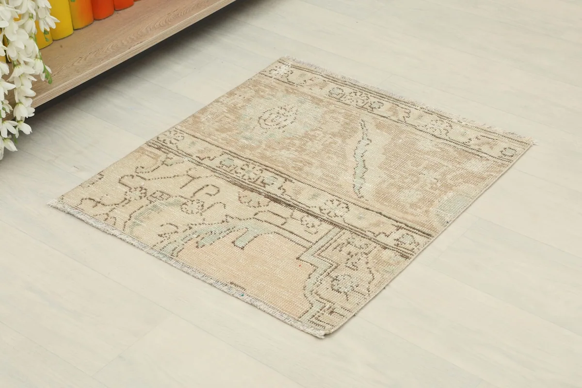 Angled view of the beige geometric doormat placed on a light floor, showing its small size