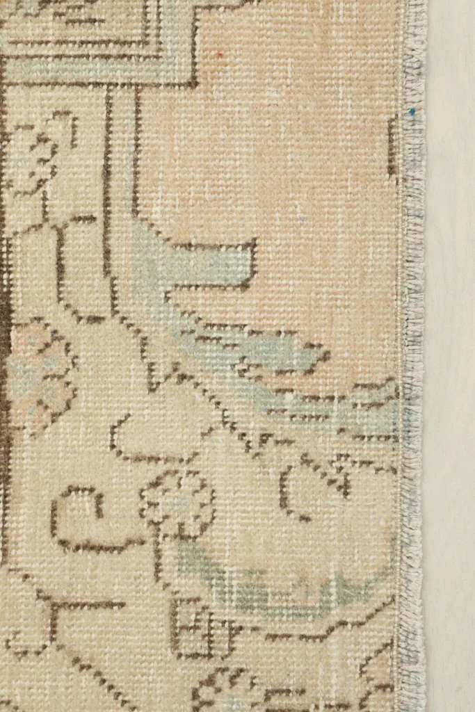 Close-up detail of the faded blue and brown geometric patterns on the beige wool pile