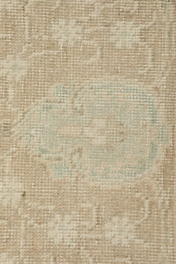Macro shot of a central faded blue geometric motif within the tan field of the rug