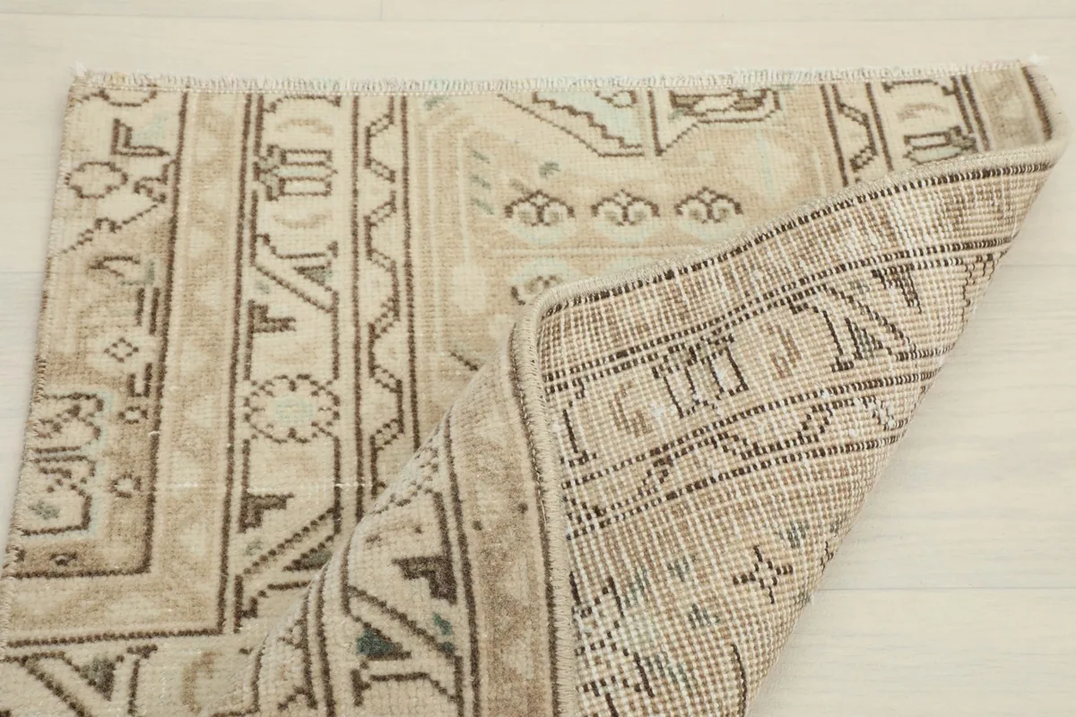Partial view of the rug with a section folded, showing the reverse side and hand knotting.