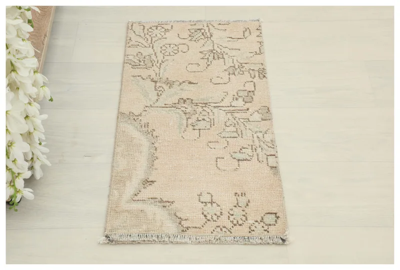 Top-down view of the 1'2" x 2'3" beige floral vintage Anatolian rug on a white floor.