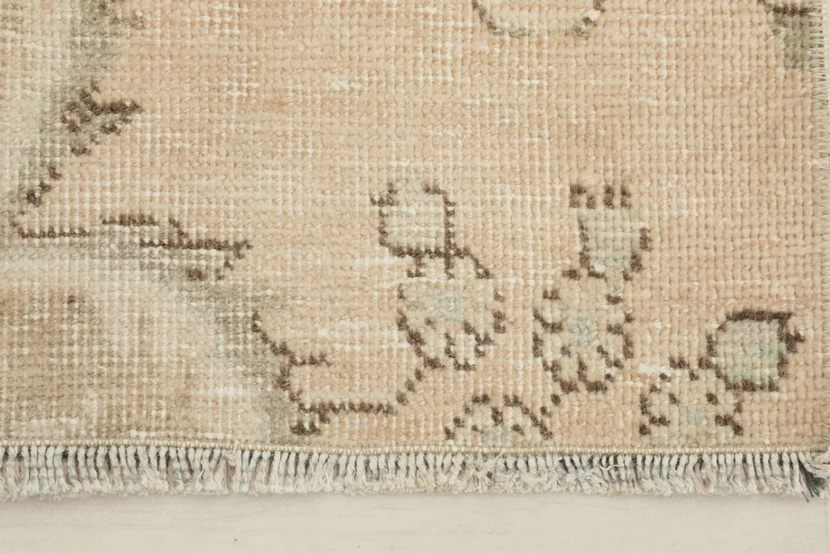 Close-up detail of the hand-knotted wool pile and faded brown and olive motifs on the rug.
