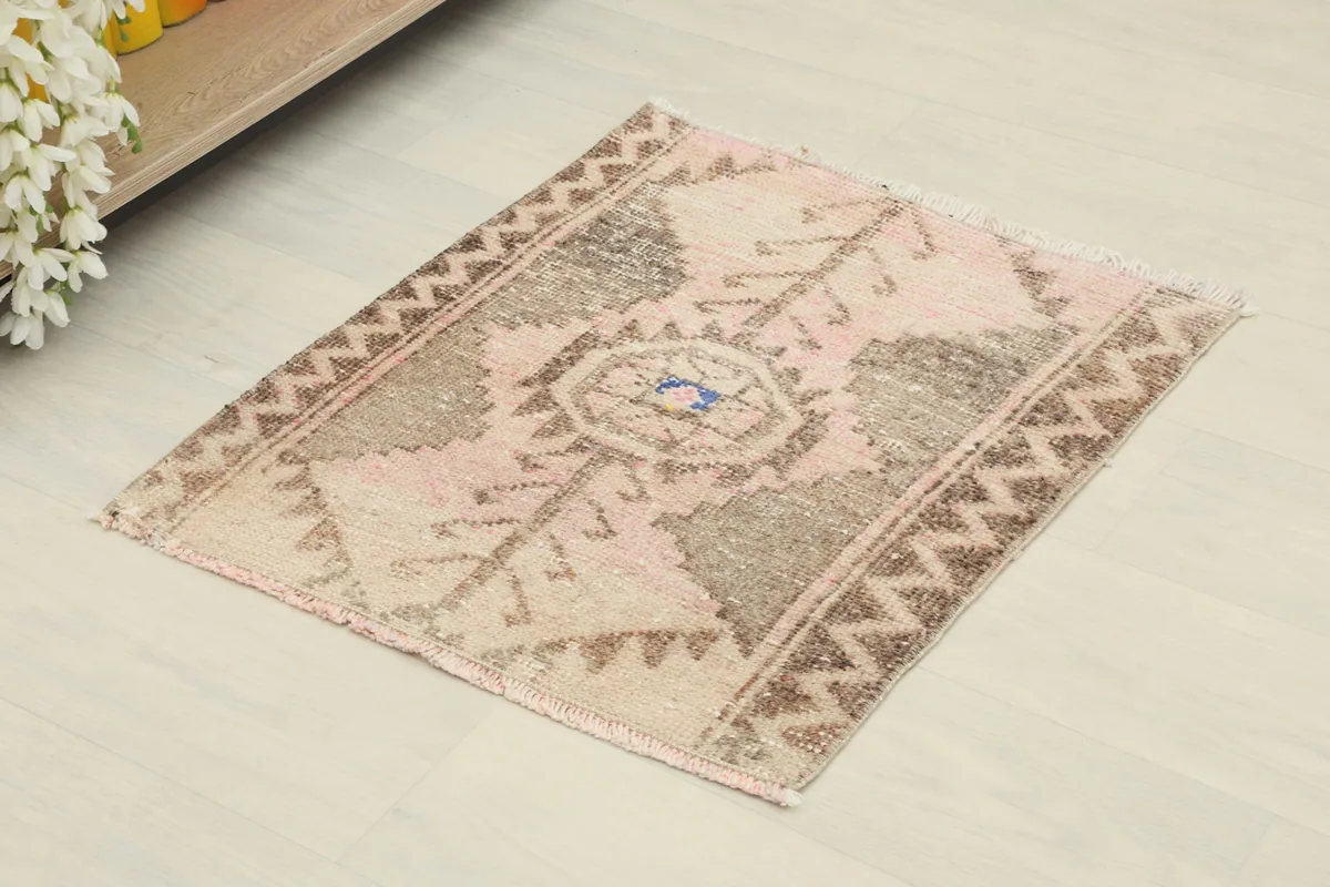 Angled view of the rose and beige tribal rug, showing its rectangular shape and pattern