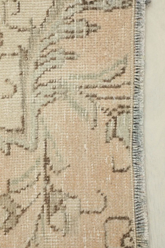 Close-up detail of the rug's border and fringe, highlighting the hand-knotted texture and muted green tones.