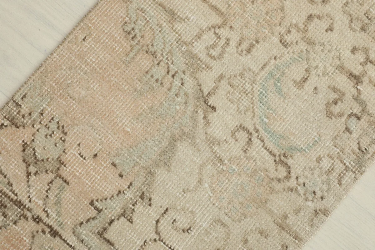 Detail shot of the rug's surface, showing the subtle color variations and abstract motifs in beige, green, and brown.