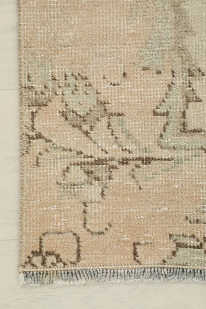 Corner detail of the rug, showcasing the faded brown outlines of the geometric patterns against the beige field.