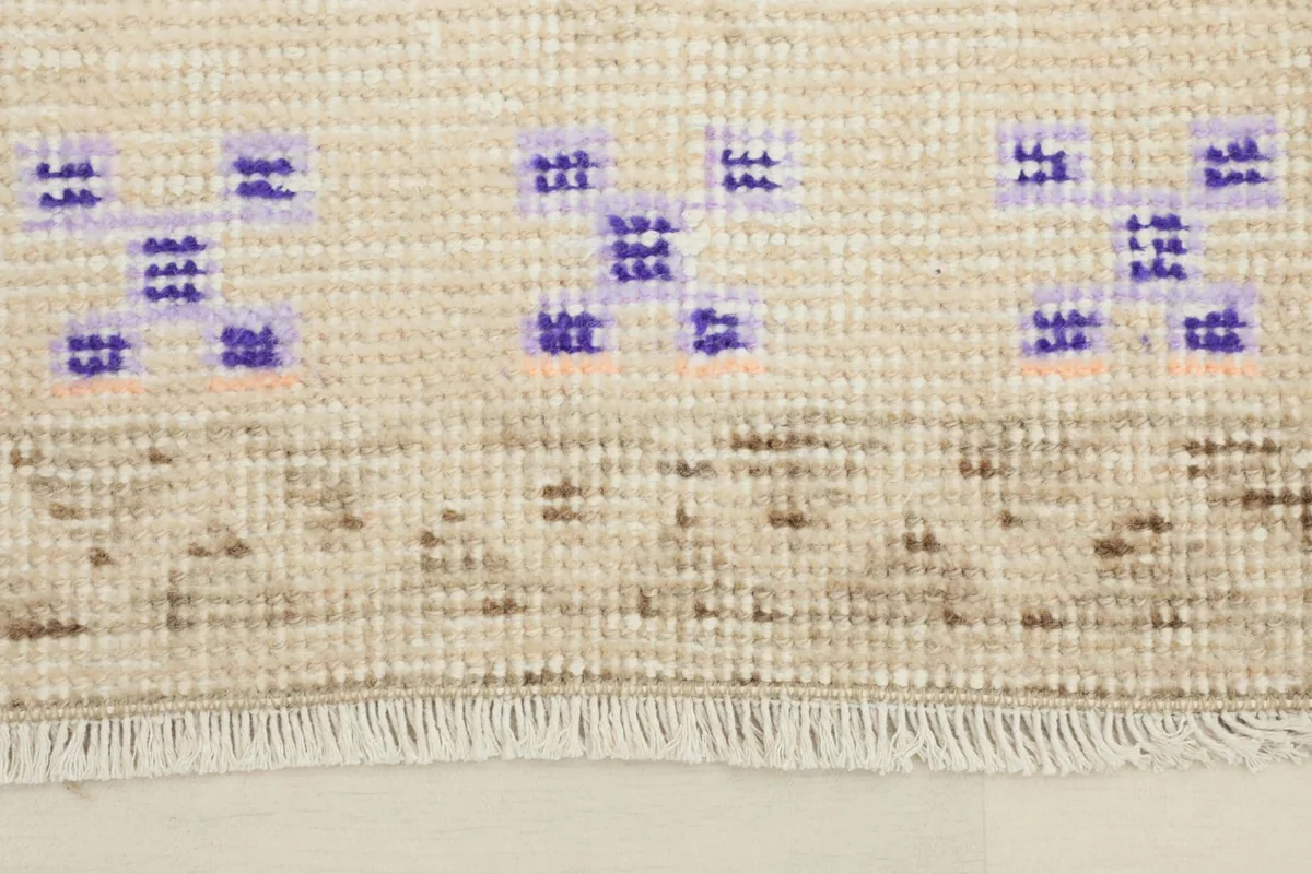 Close-up of the rug's fringe and a section of the beige field with purple motifs