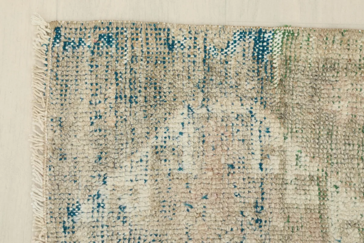 Corner detail showing the distressed blue and beige tones and fringe of the hand-knotted rug.