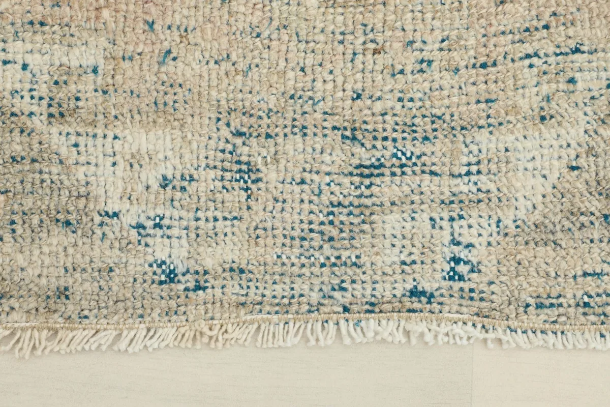 Close-up detail of the low pile texture and distressed blue and beige colors of the vintage rug.