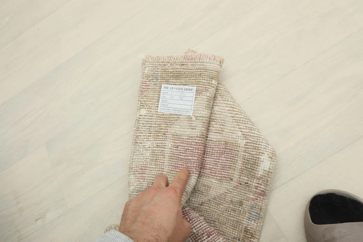 The rug partially folded to show the label and scale, with a person's hand for reference.
