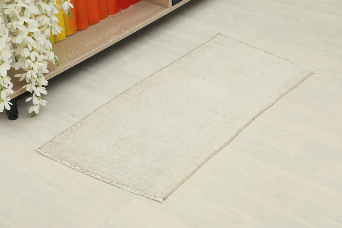 Overhead view of the ivory doormat placed on a light floor next to a wooden shelf.