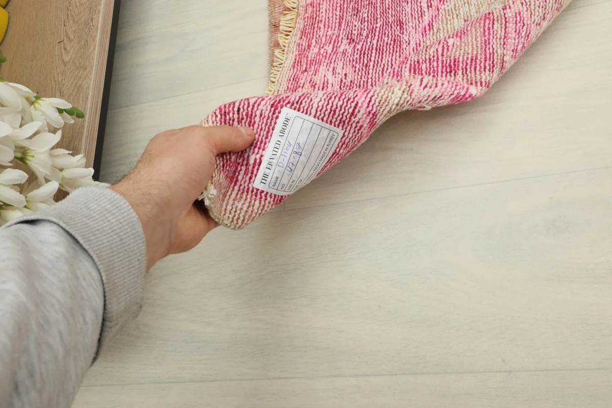 Hand holding the rug, showing the back of the hand-knotted construction and tag